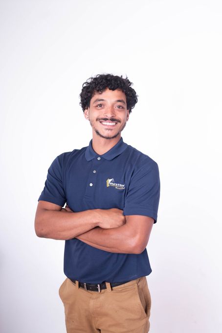 Smiling person in a navy polo and khaki pants with arms crossed against a white background