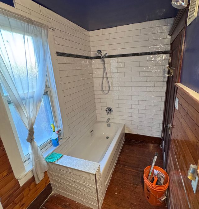 Bathroom renovation: white subway tile, dark wood, blue ceiling, bathtub, showerhead, window with curtains.