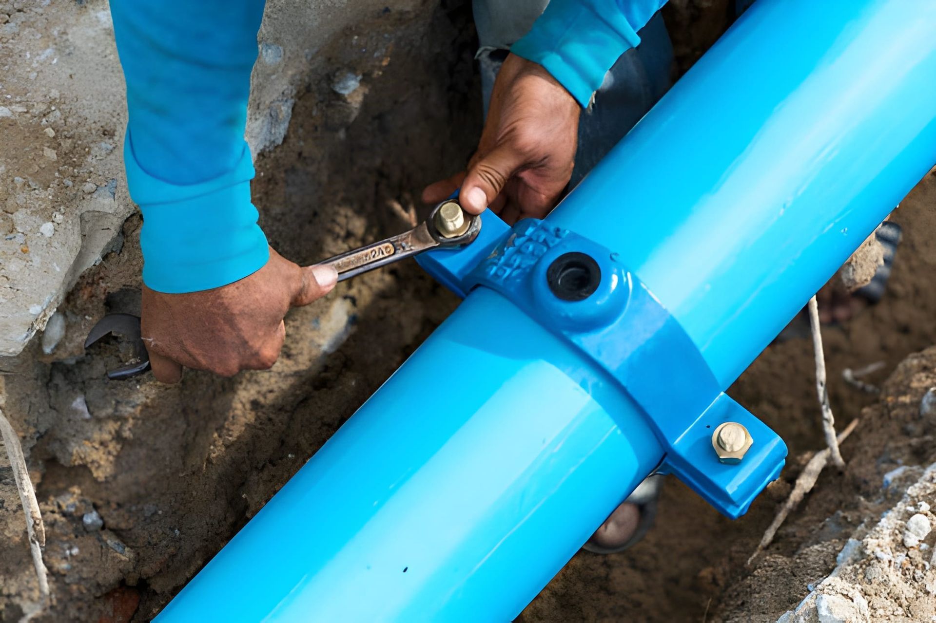 Hands of a person using a wrench to tighten a bolt on a blue pipe clamp.