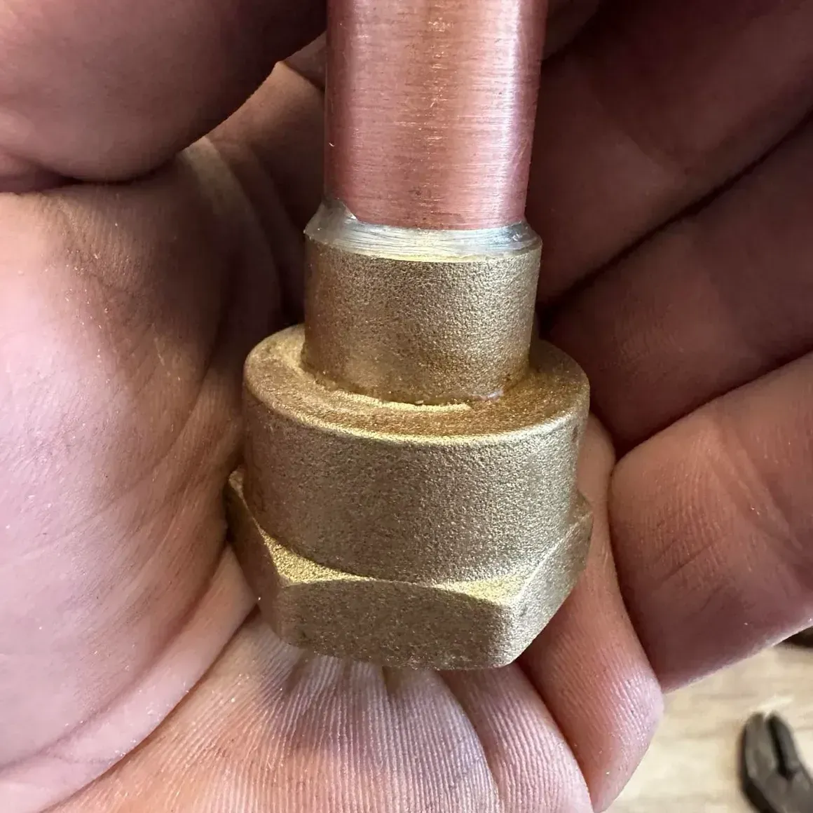 Copper pipe connected to a brass fitting with visible solder, held in hand.