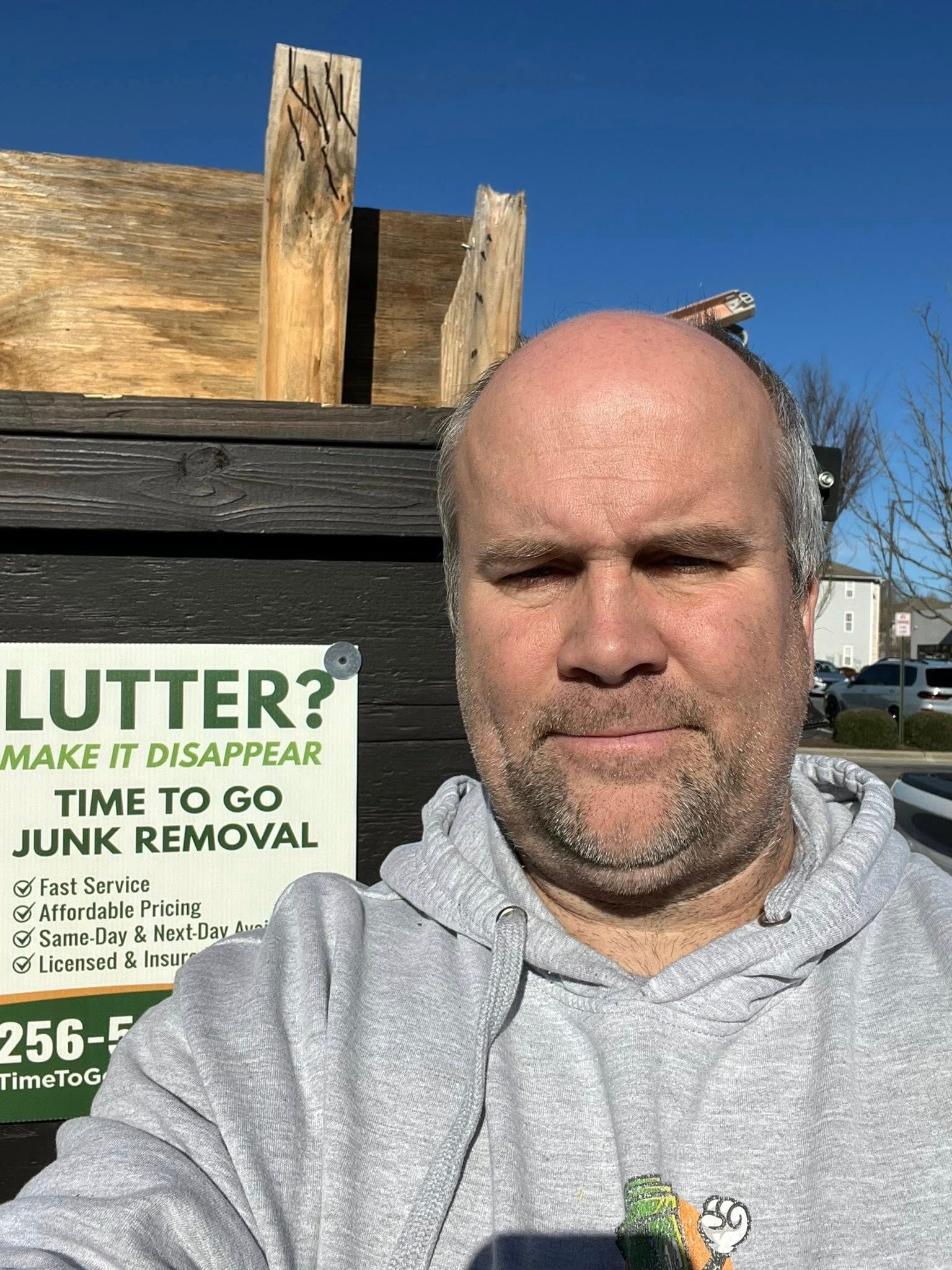 A person in a gray hoodie takes a selfie in front of a dumpster with a 