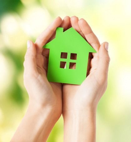 Hands holding a green house cutout against a blurred bright background