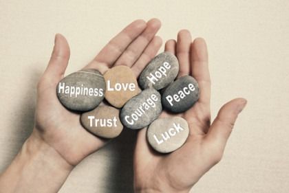 Hands holding stones labeled happiness, love, hope, trust, courage, peace, and luck