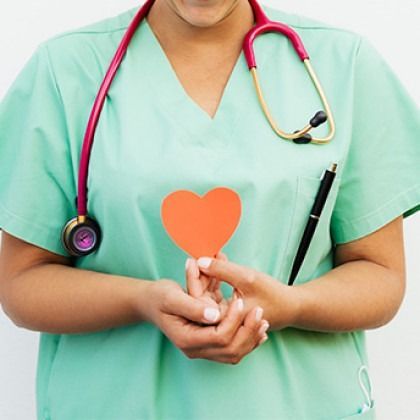Nurse in teal scrubs holding a red heart icon, with a stethoscope around the neck
