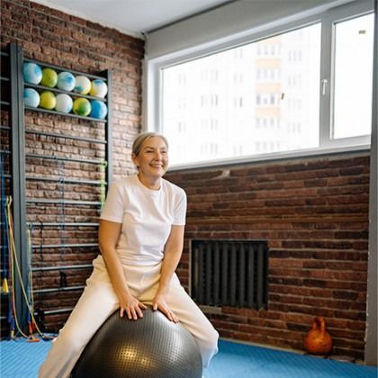 Person smiling on a stability ball in a studio with brick walls and exercise equipment