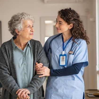 Nurse in blue scrubs gently supports an older patient in a hospital hallway