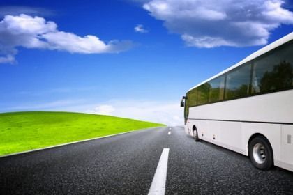 White bus on an open road beside green hills under a blue sky