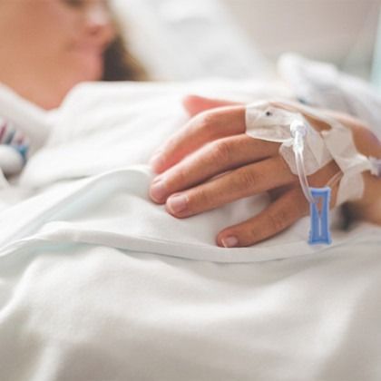 Hand resting on white hospital bedding with IV line and blue clip attached