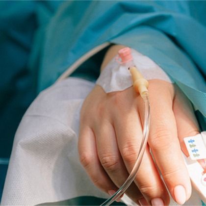 Hand with IV catheter under a blue hospital blanket