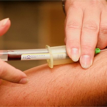Hands holding a syringe and injecting a forearm with a green-capped needle