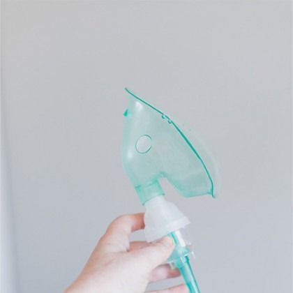 Hand holding a turquoise nebulizer mask against a light gray background