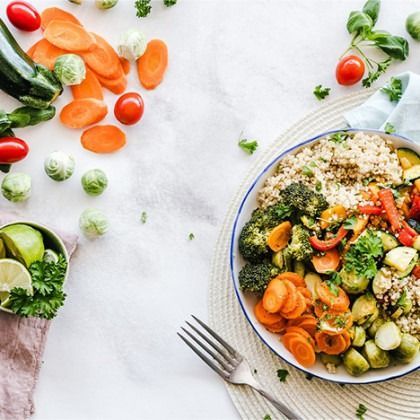 Colorful grain bowl with broccoli, carrots, cucumbers, tomatoes, and avocado on a white table