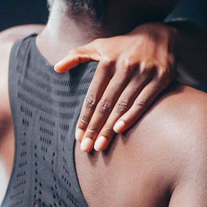 Hand resting on a shoulder in a close-up of a person wearing a dark athletic tank top