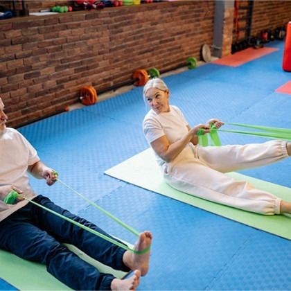 Two people doing seated resistance band exercises on mats in a gym