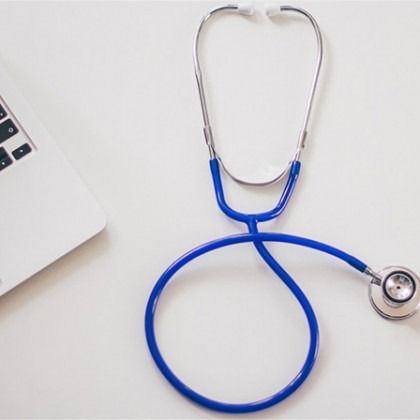 Blue stethoscope on a white desk beside a laptop corner