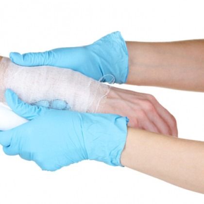 Blue-gloved hands wrapping a white bandage around a forearm