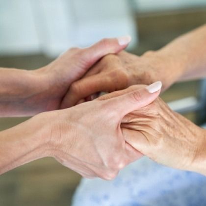 Two hands gently holding an elderly person's hand in a supportive gesture