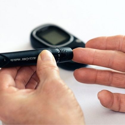 Person pricking a finger with a glucose meter lancet next to a blood sugar monitor