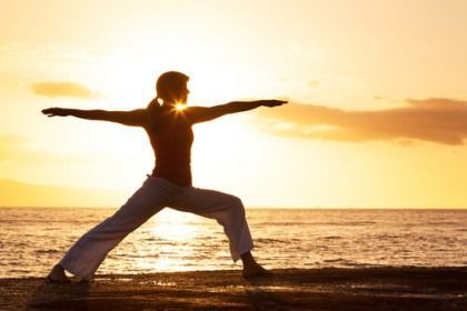 Silhouette of a person in a warrior yoga pose on a beach at sunset