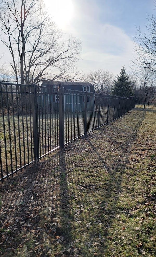 A black metal fence surrounds a grassy field with a house in the background.