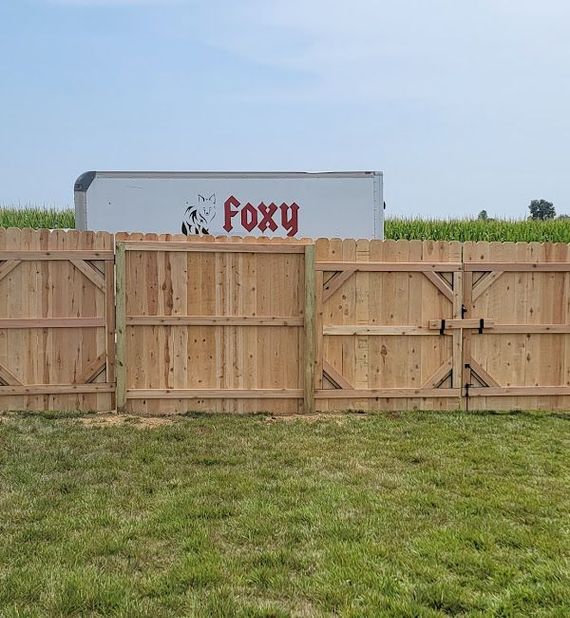 A wooden fence in a grassy field with a foxy truck in the background.