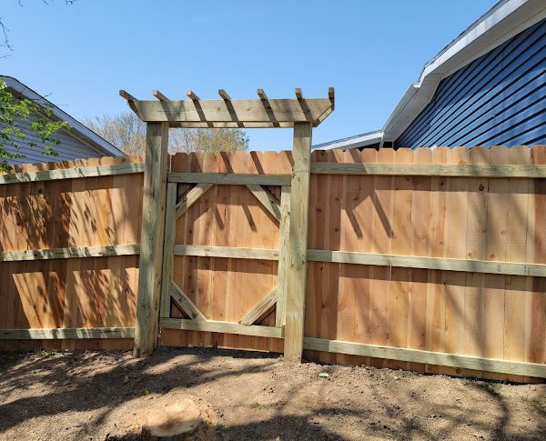 A wooden fence with a gate and a pergola attached to it.
