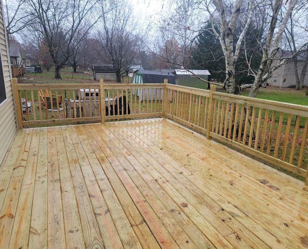 A large wooden deck with a railing and trees in the background.