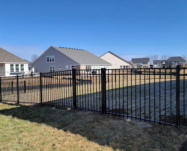 A metal fence surrounds a grassy field with houses in the background.
