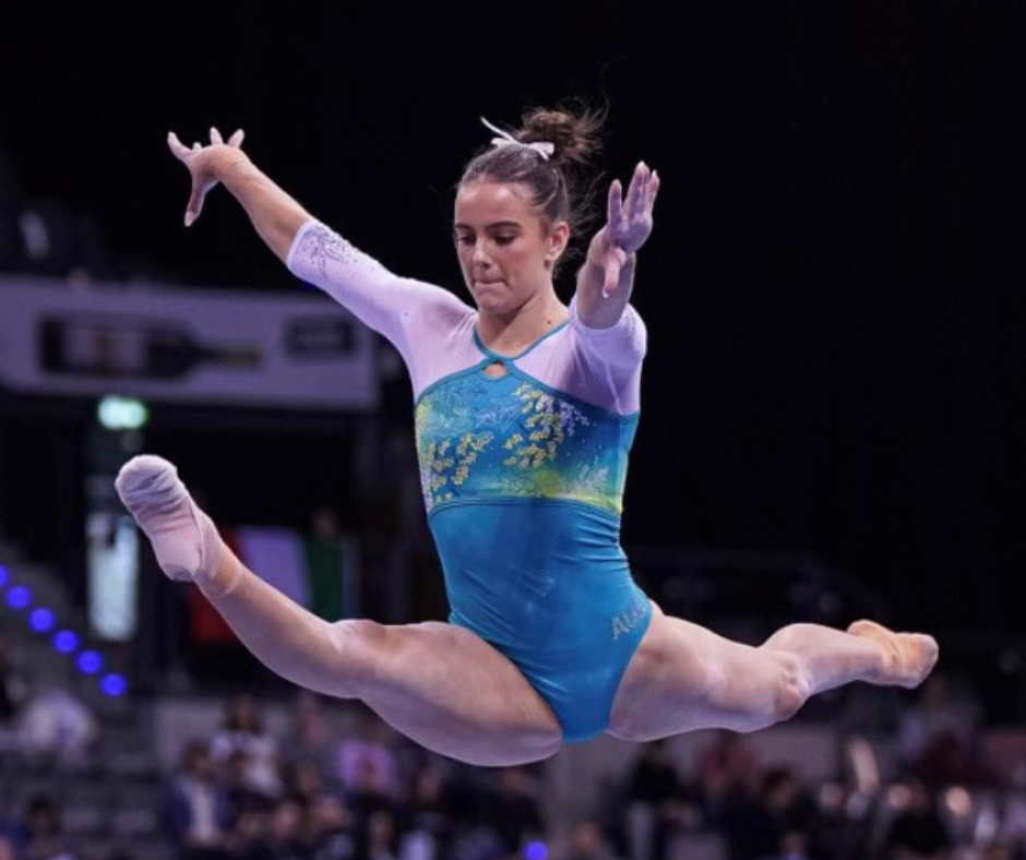 Gymnast in mid-air split, wearing blue and white leotard, performing a floor routine.