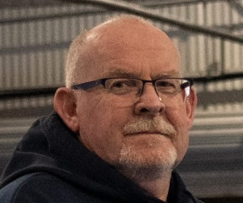 A bald man with glasses and a beard is wearing a black hoodie.