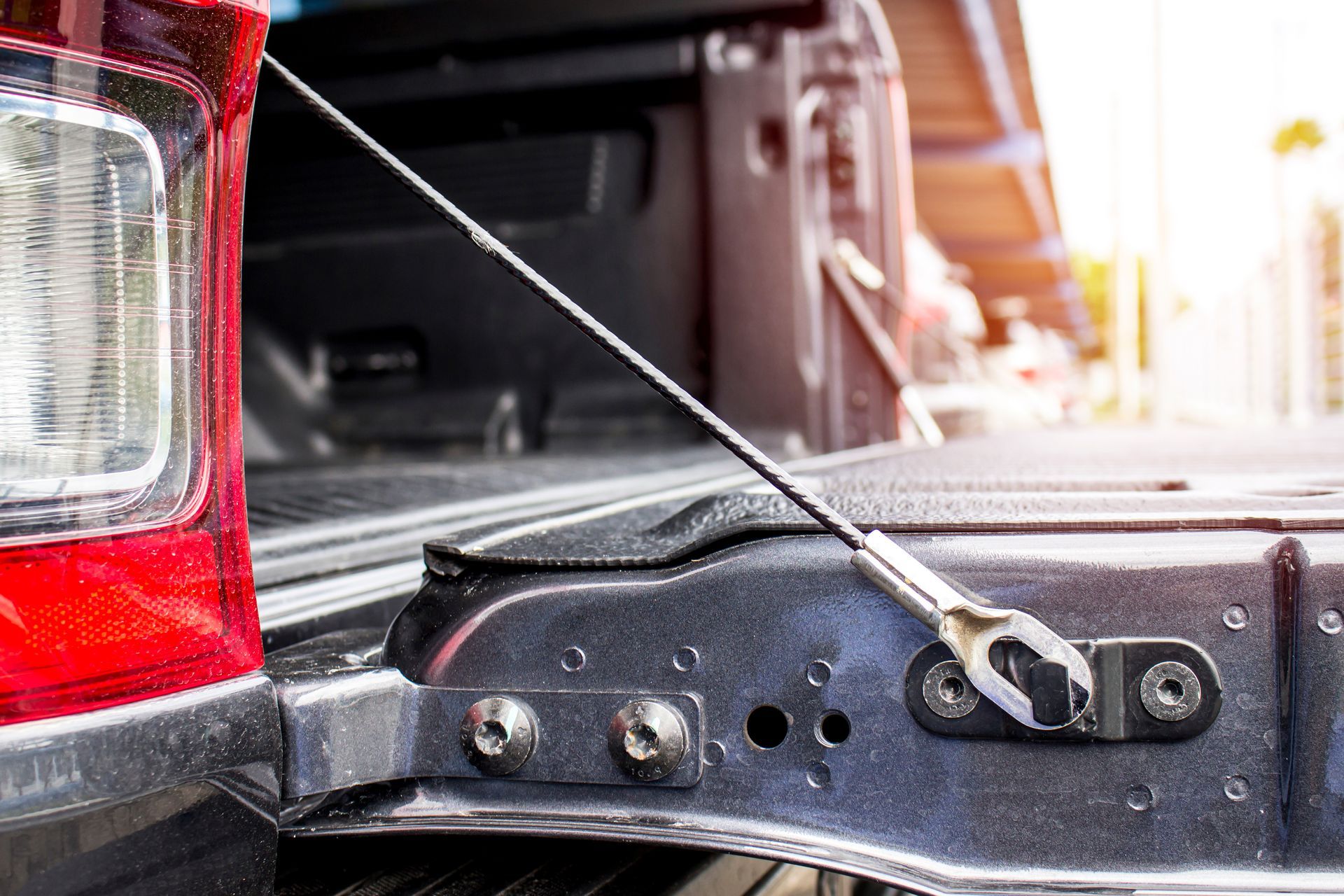 Close-up of a pickup truck tailgate hinge and cable support beside a rear light.