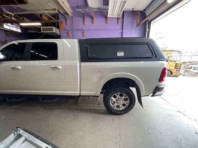 White pickup truck with a black camper shell inside a garage.
