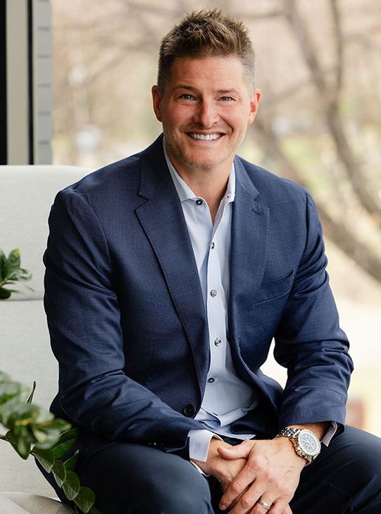 Smiling man in a gray suit sitting against a dark background