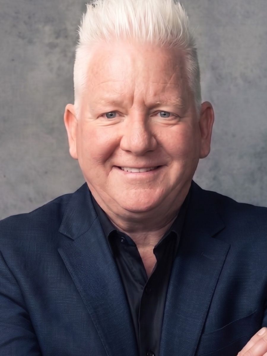 Smiling person in a navy blazer against a gray studio background
