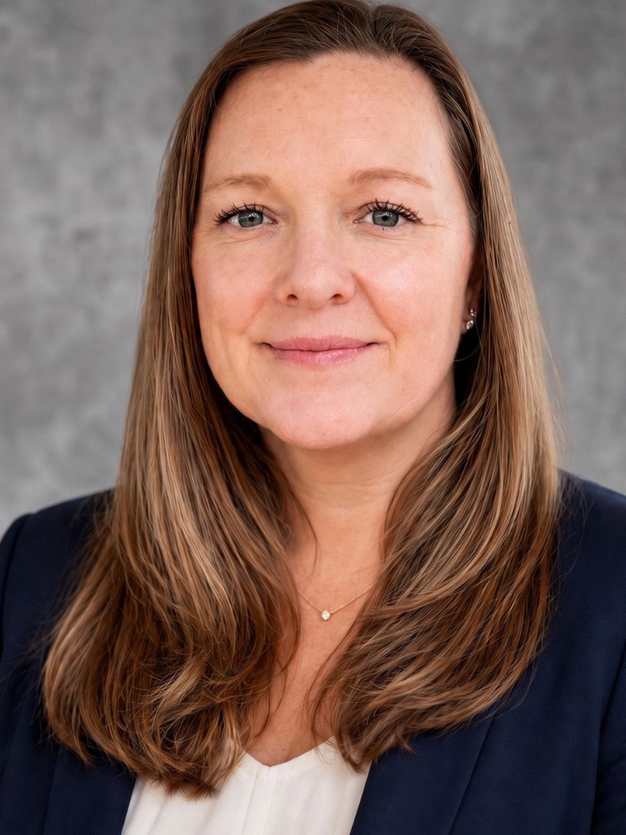 Smiling person in a navy blazer against a gray studio background