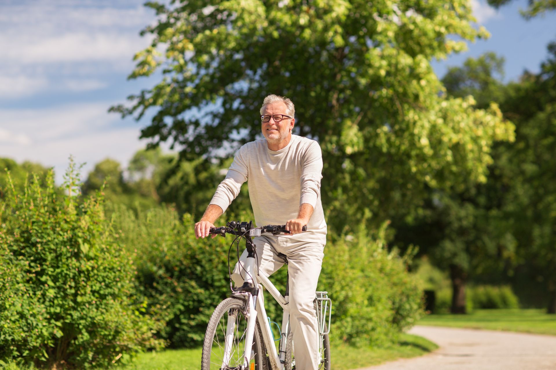 Man riding a bicycle on a sunlit path beside green hedges and trees