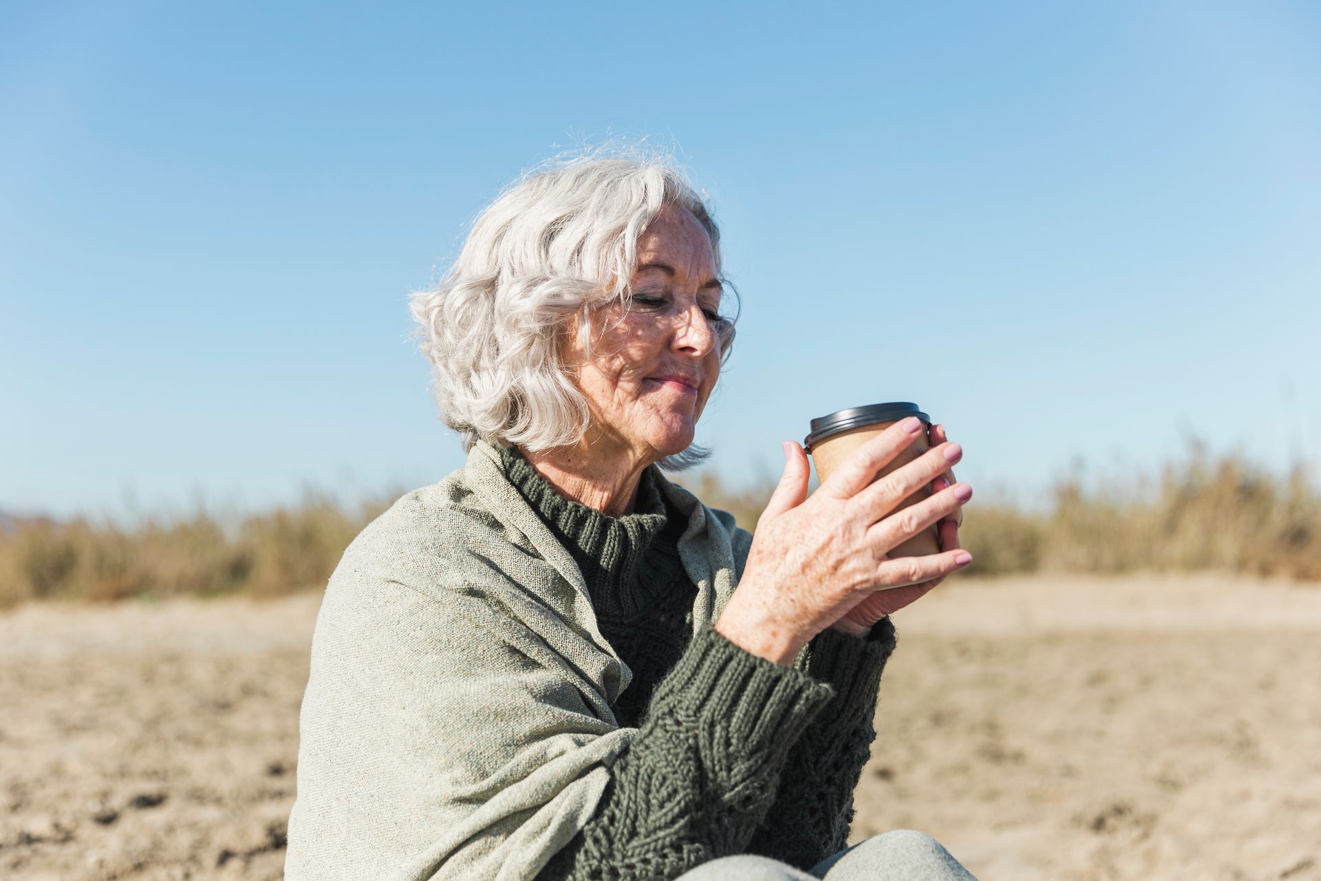 Person with white hair holding a cup outdoors on a sunny beach