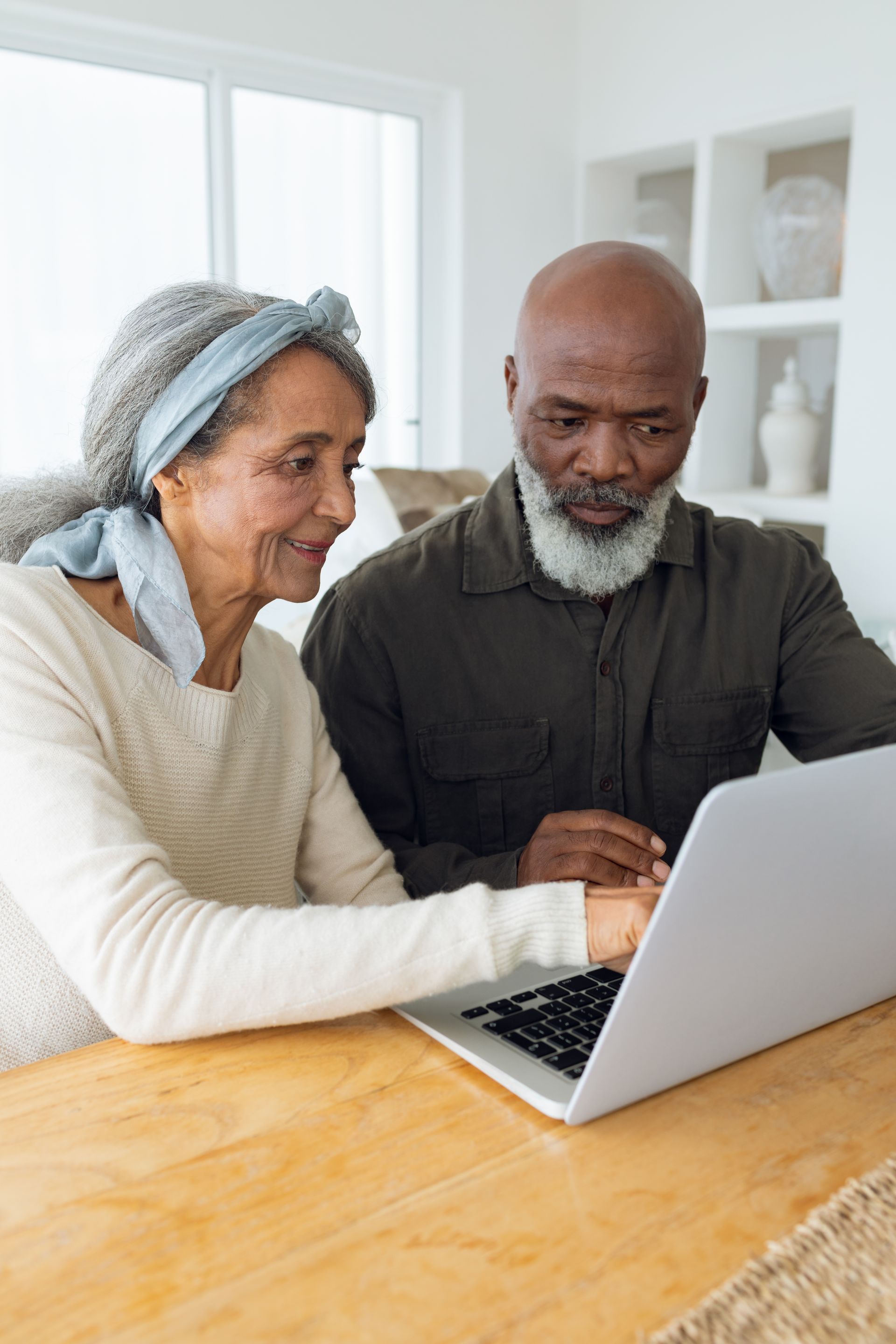 Two people smiling and using a laptop at a wooden table in a bright room