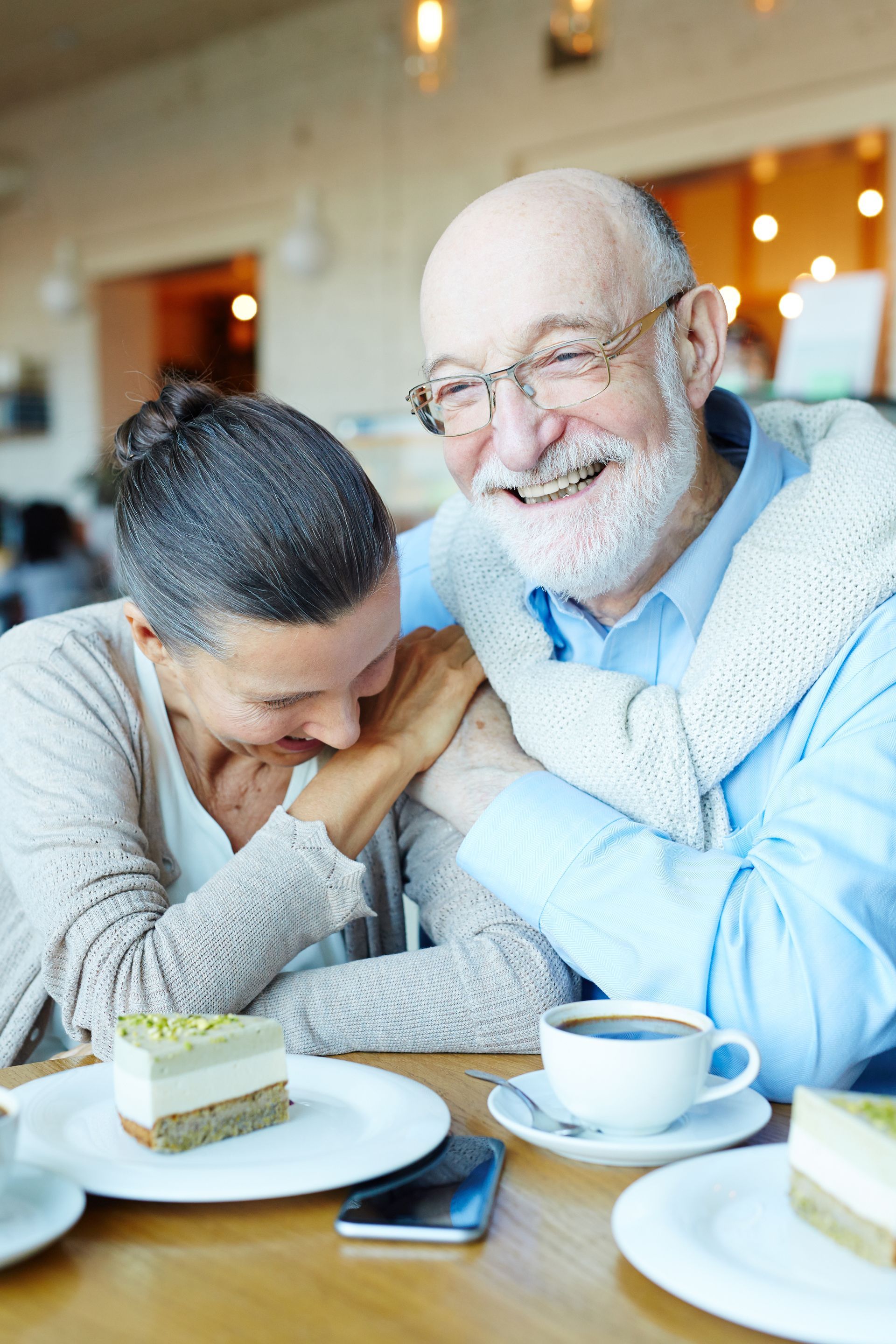 Two people smiling and leaning together at a café table with tea and cake