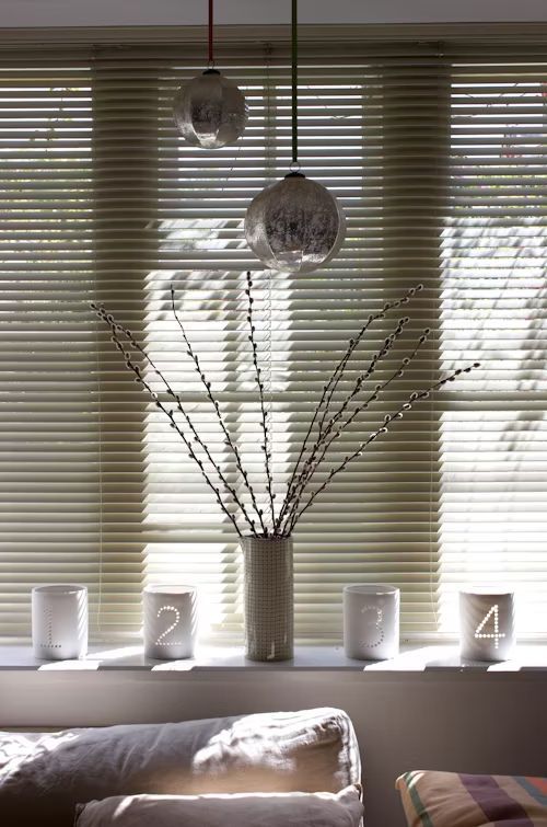 Window sill decorated with pussy willow branches, candles with numbers, and hanging glass ornaments