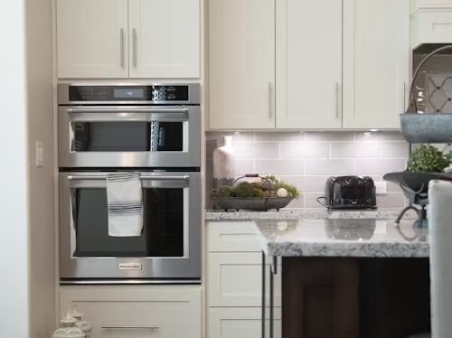 Built-in stainless steel double oven in a cream-colored kitchen with matching cabinets and granite countertops.