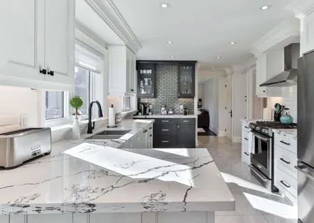 Bright white modern kitchen with marble countertop, stainless steel appliances, and black accents.