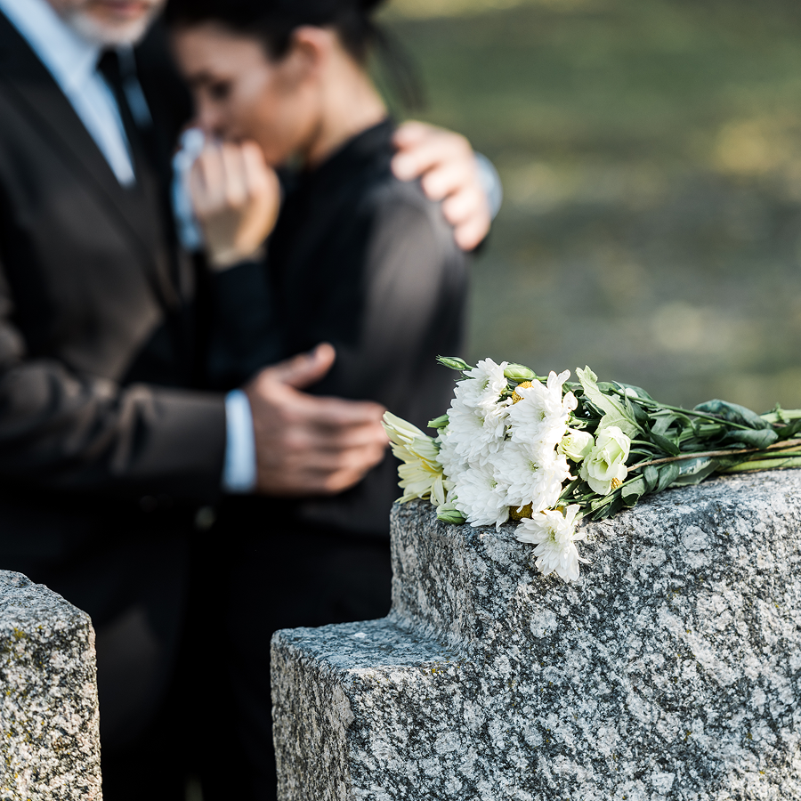 A man and woman are standing next to a grave with flowers.