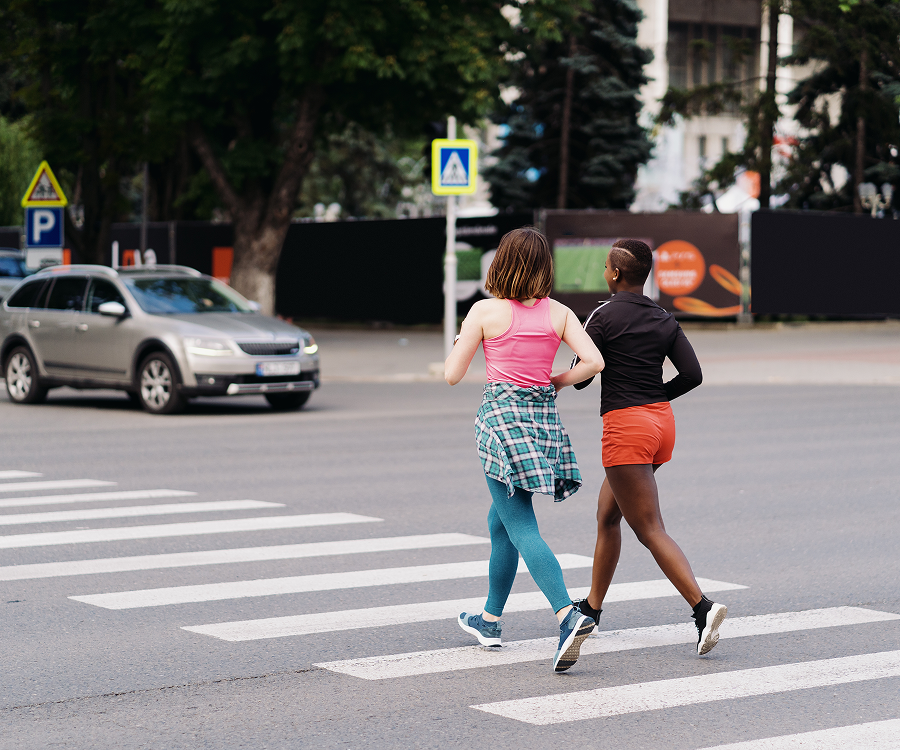 Two women are crossing the street while a car is driving by.