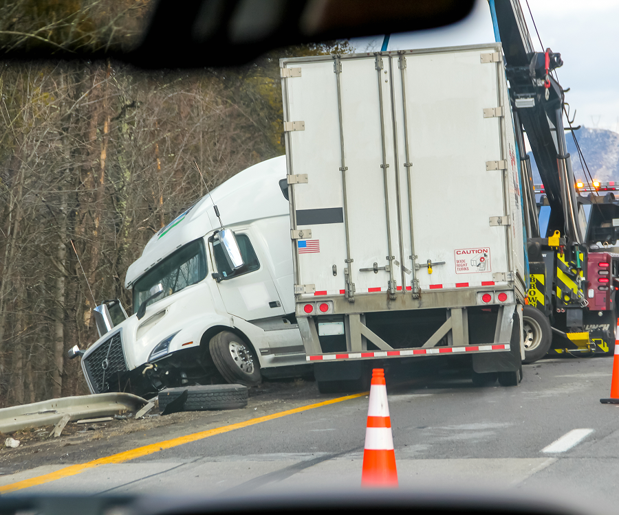 A semi truck is being towed by a crane on the side of the road