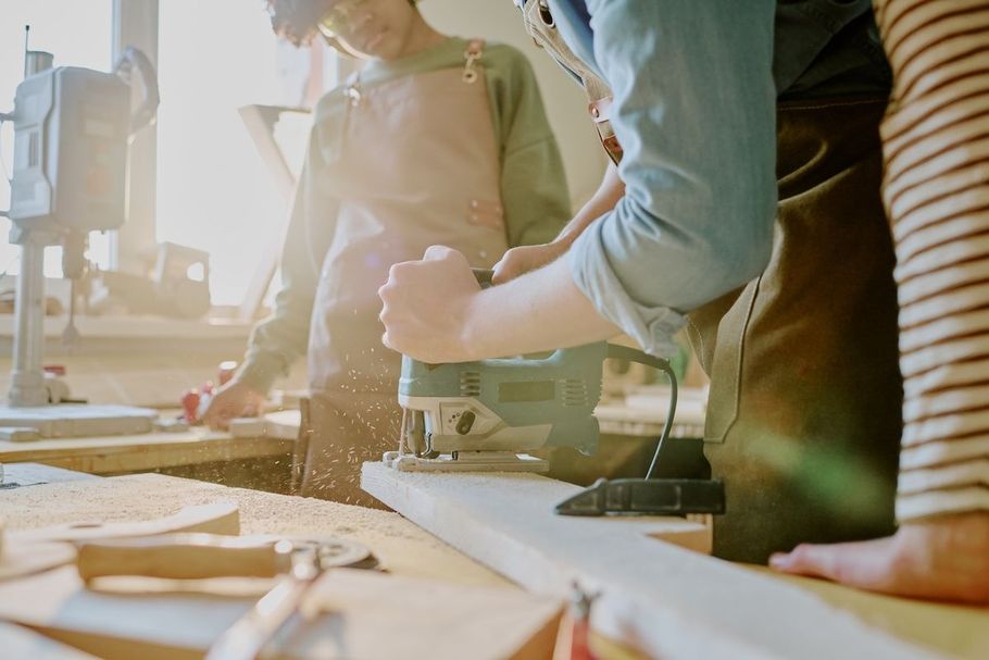 People using power tools to work on wood in a bright workshop