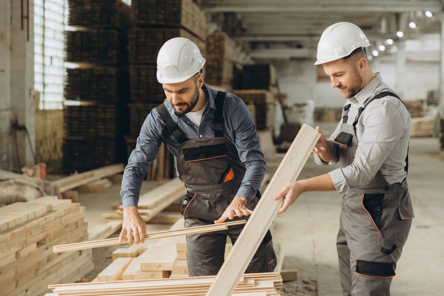 Two workers in hard hats measuring wood in a lumber workshop