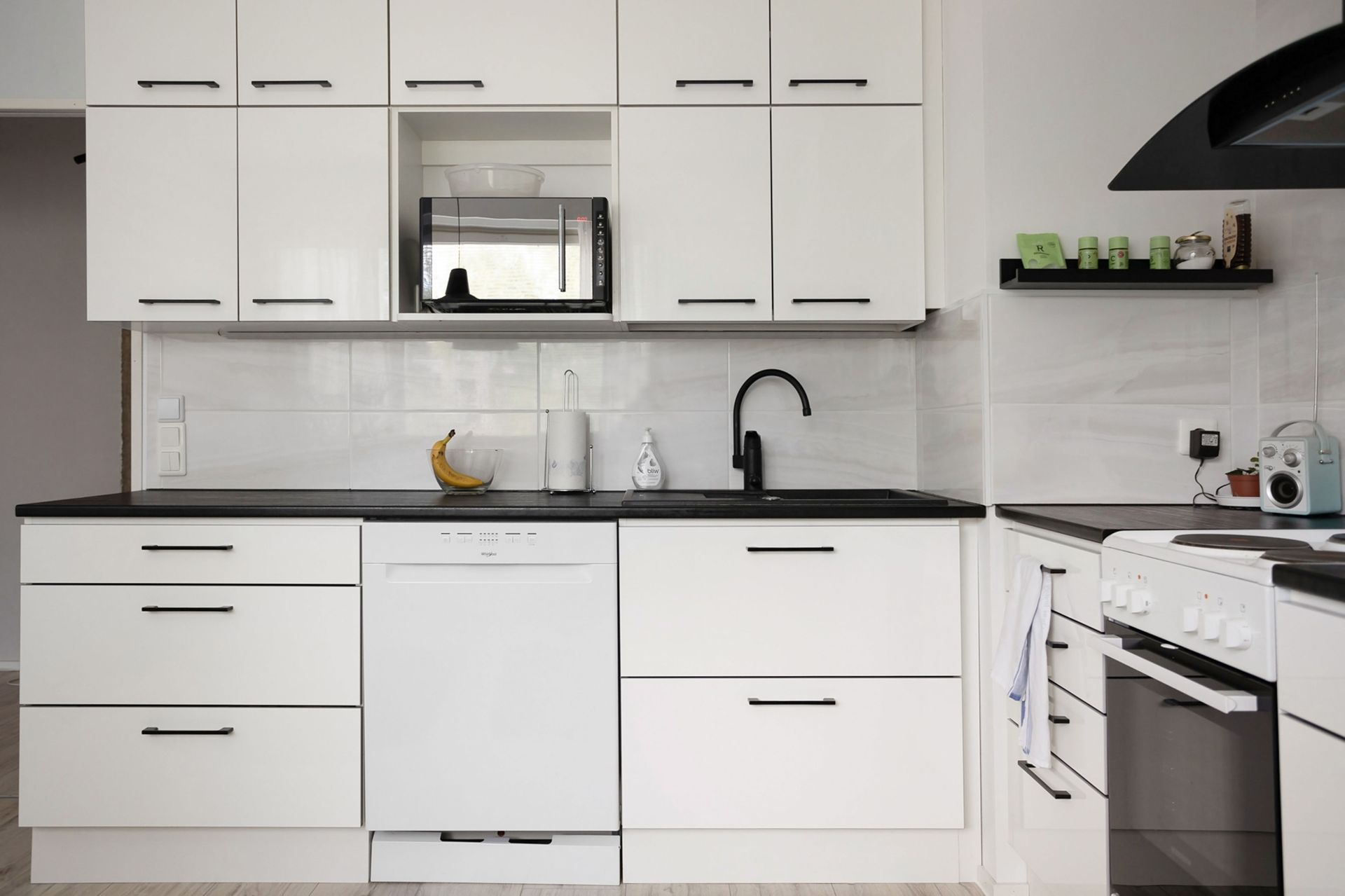 Modern white kitchen with black countertops, white cabinets, sink, dishwasher, and oven; microwave on the counter.