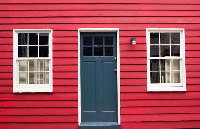 Red house exterior with a blue door and two white-trimmed windows