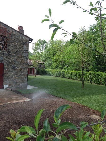 Un irrigatore spruzza acqua su un prato verde lussureggiante di fronte a un edificio in pietra